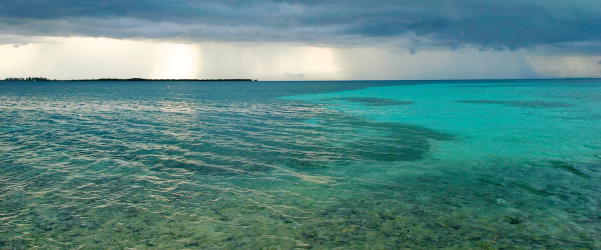 A turquoise sea with clear shallow waters and a distant landmass under a cloudy sky.