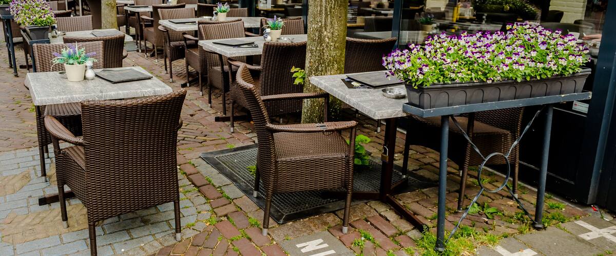 An outdoor café with wicker furniture, tables, and potted plants.