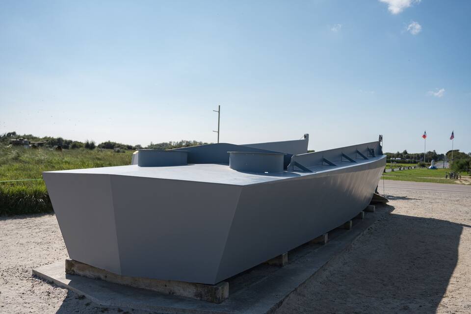Una escultura moderna de barco sobre una plataforma de hormigón, con cielo despejado al fondo.