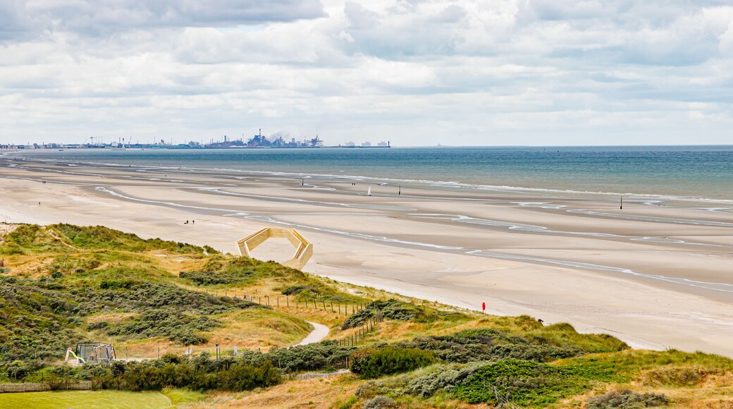 Panoramic landscape of beach with North Sea and industrial complex in Dunkirk, France in background, stormy sky covered with clouds, viewpoint and dunes, cloudy day De Panne, West Flanders, Belgium