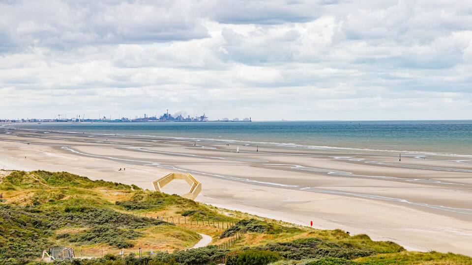Panoramic landscape of beach with North Sea and industrial complex in Dunkirk, France in background, stormy sky covered with clouds, viewpoint and dunes, cloudy day De Panne, West Flanders, Belgium