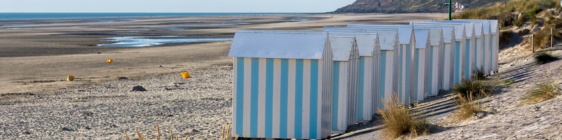 Cabañas de playa, una playa arenosa y una colina distante con edificios.