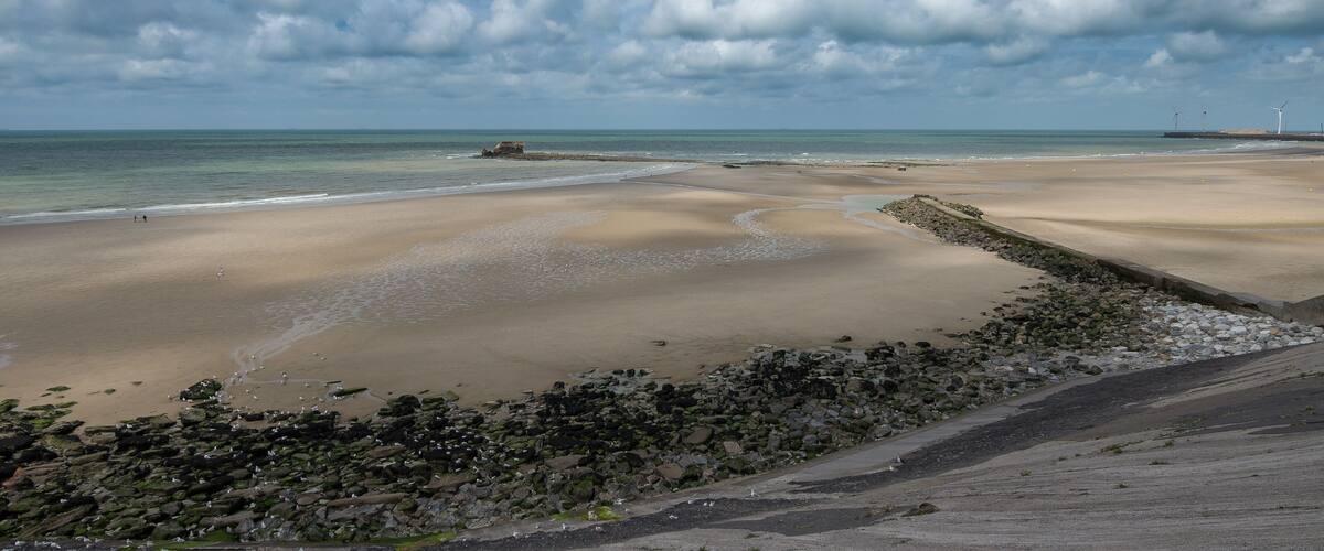 A sandy beach with a rocky shoreline, calm sea, and overcast sky.