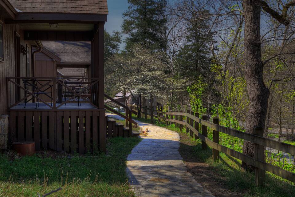 A wooden deck with chairs and a stone path leading through a forest.