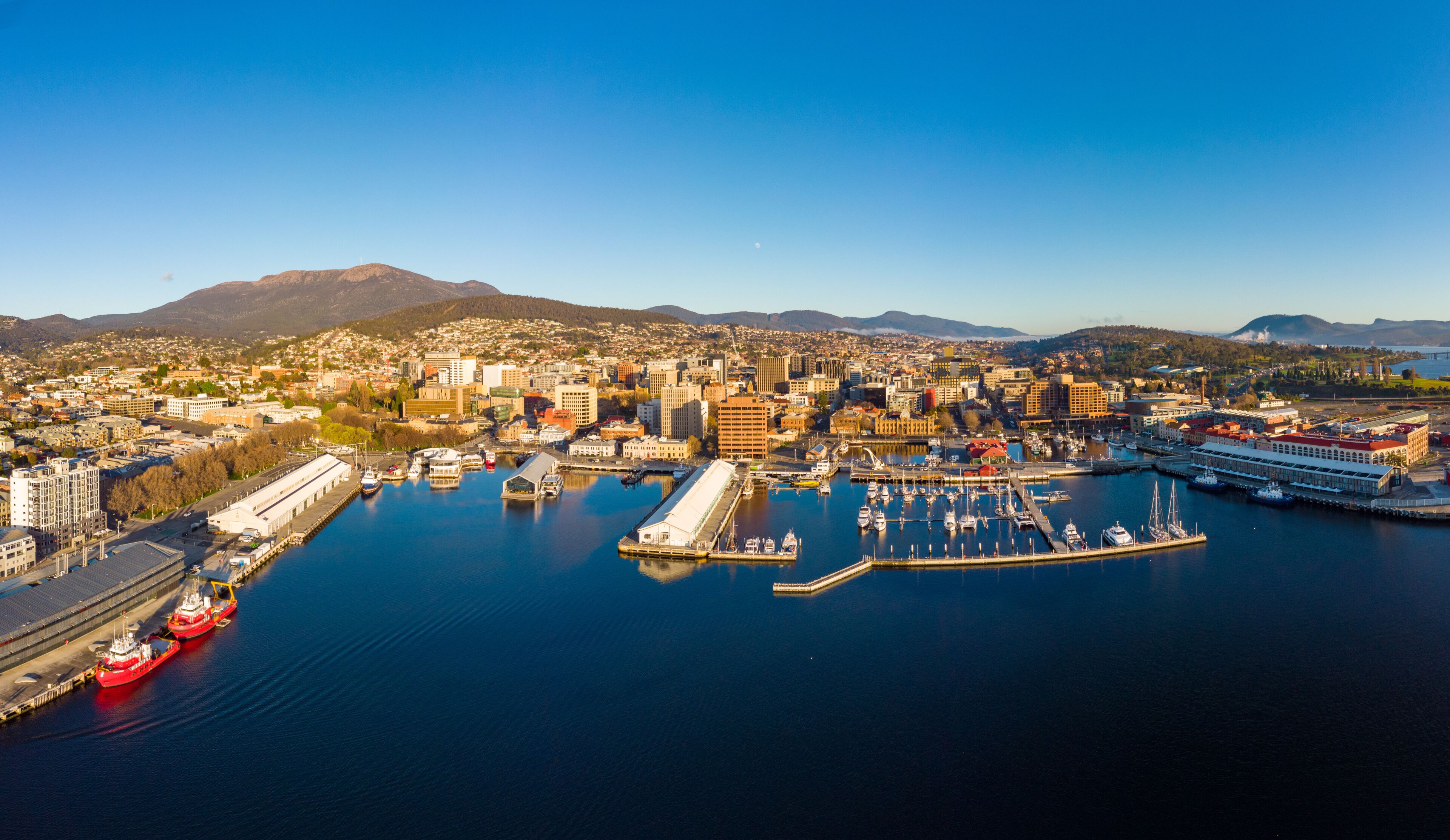 A coastal city with a marina, ships, and mountains in the background.