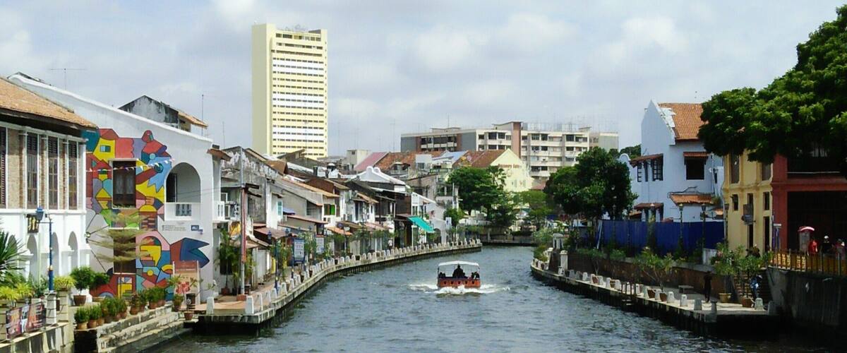 A river with a boat, colorful buildings, and a tall skyscraper in the background.