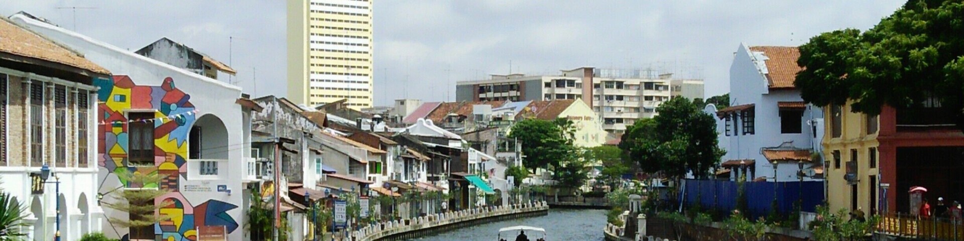 A river with a boat, colorful buildings, and a tall skyscraper in the background.