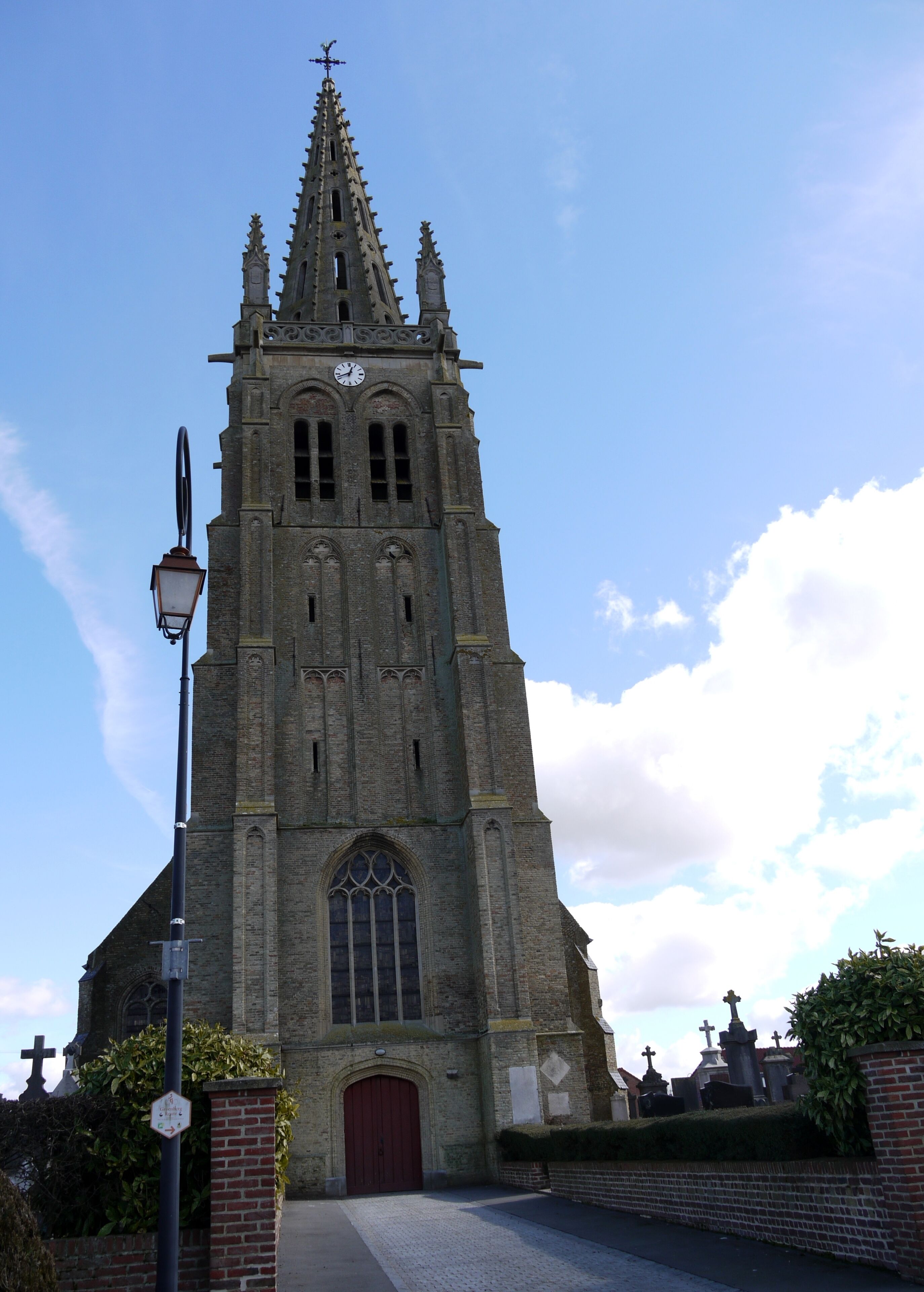 A tall church with a clock tower, a red door, and crosses in the background.