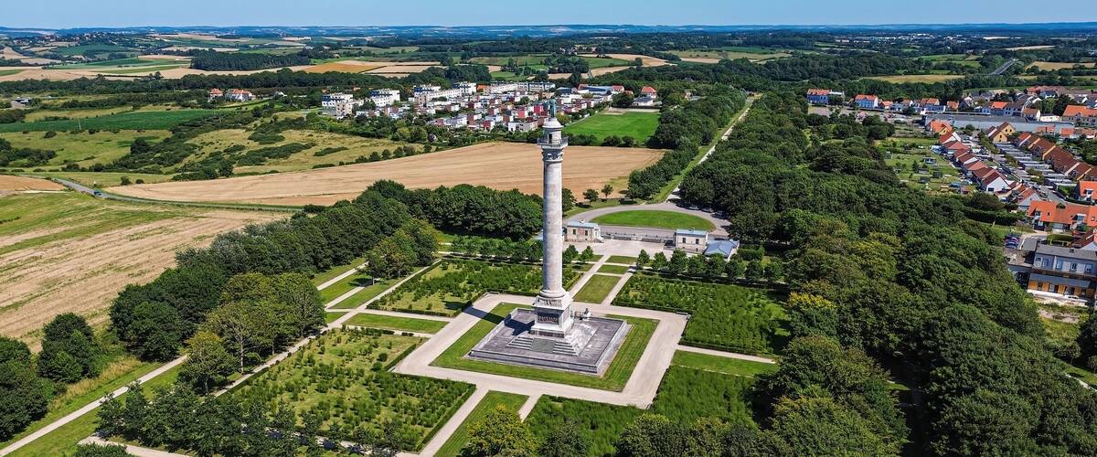 An aerial view of a town with a prominent tower, surrounded by fields, residential areas, and a clear sky.