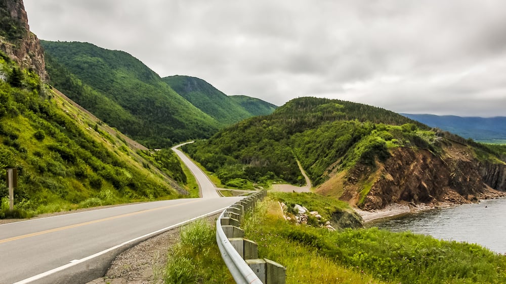 A winding road along a coastal cliffside with lush greenery and a view of the ocean.