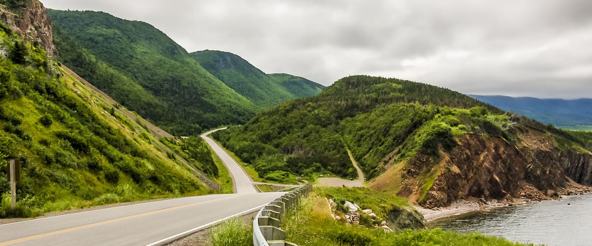 A winding road along a coastal cliffside with lush greenery and a view of the ocean.