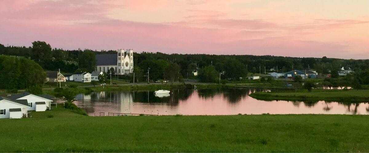 A serene lakeside town with a prominent church, a small boat on the water, and lush greenery.