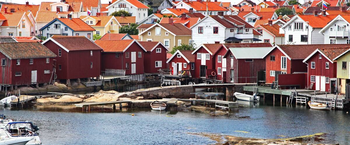 A harbor with red and white buildings, boats, and a rocky shoreline.