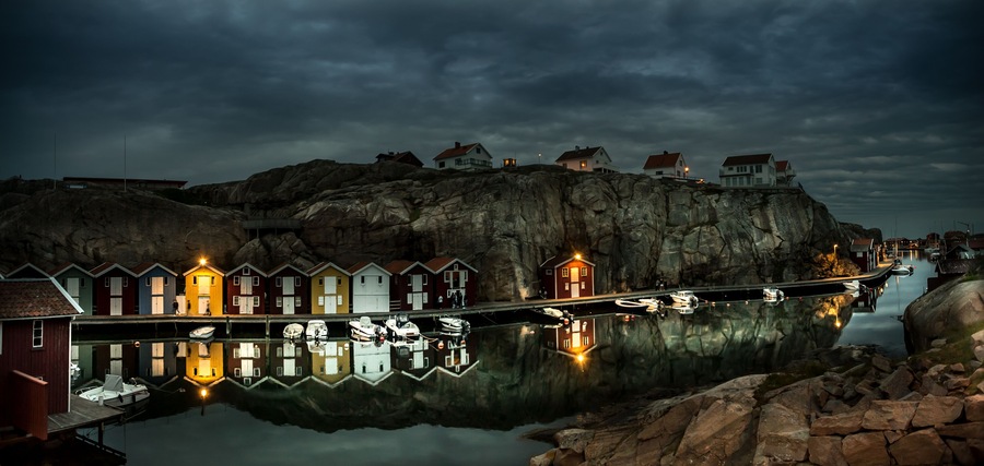 Um cais com casas coloridas e barcos refletidos em águas calmas.