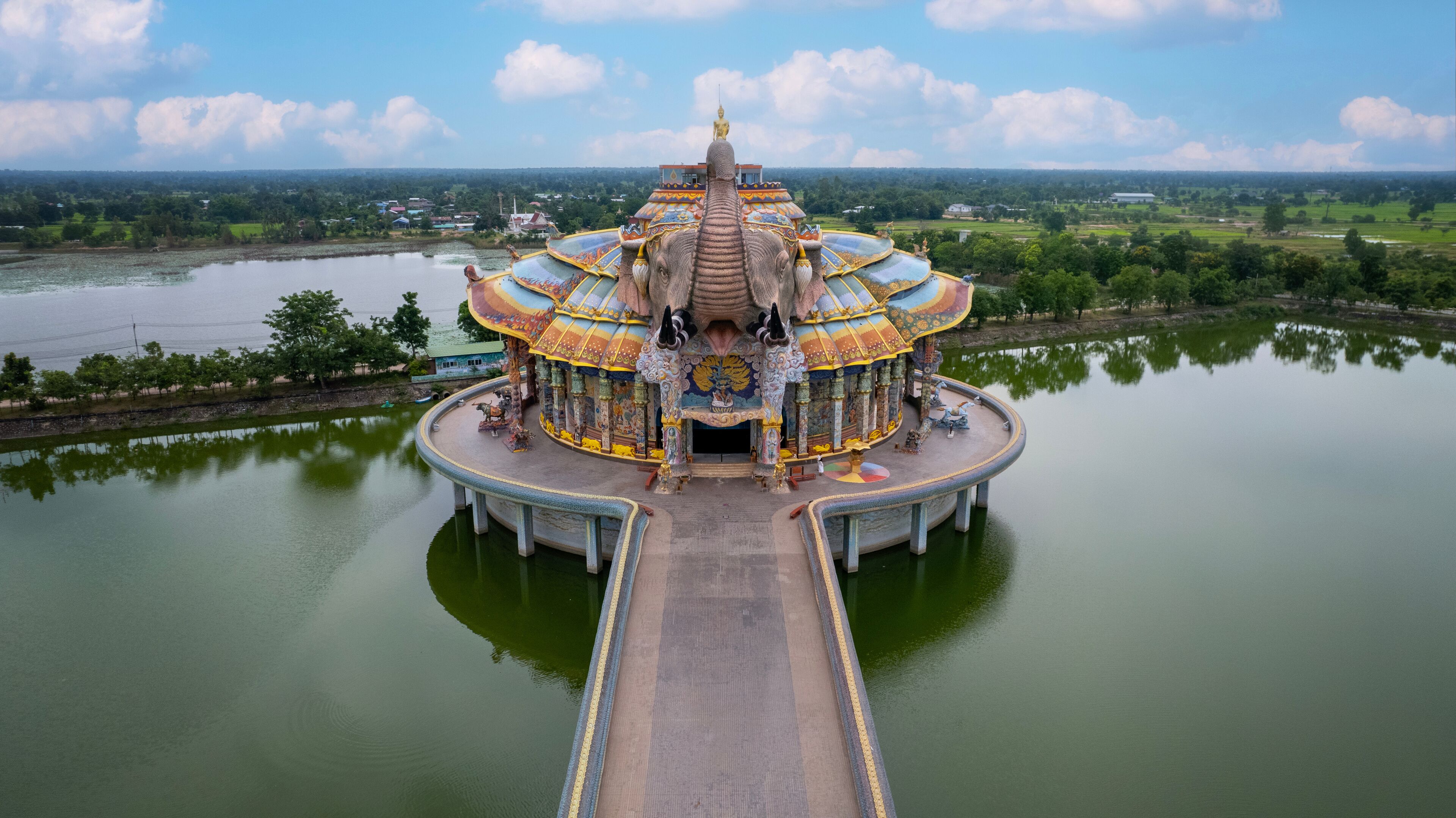 A temple with a golden statue on top, surrounded by a body of water and greenery.