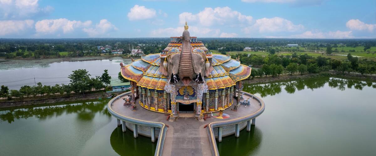 A temple with a golden statue on top, surrounded by a body of water and greenery.