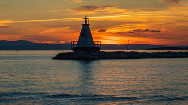 banner photo of kayakers approaching the Lake Champlain breakwater's lighthouse with a sea bird perched on the top at sunset