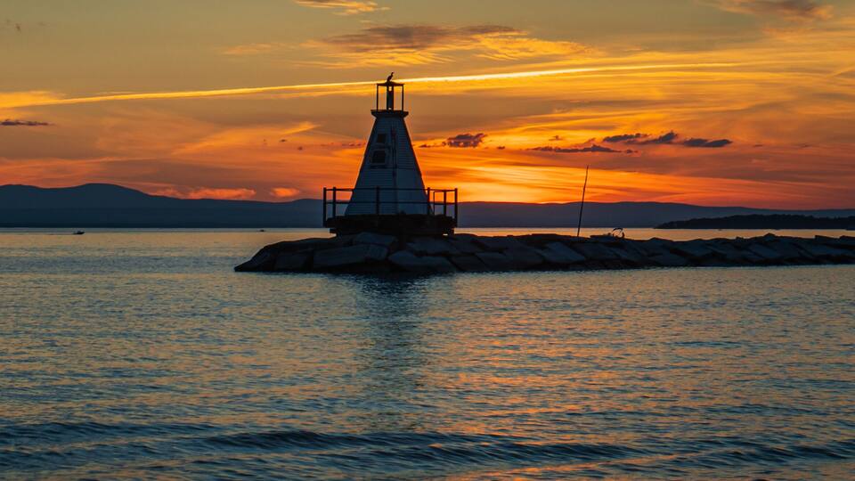 A lighthouse on a rocky outcrop with a sunset in the background.
