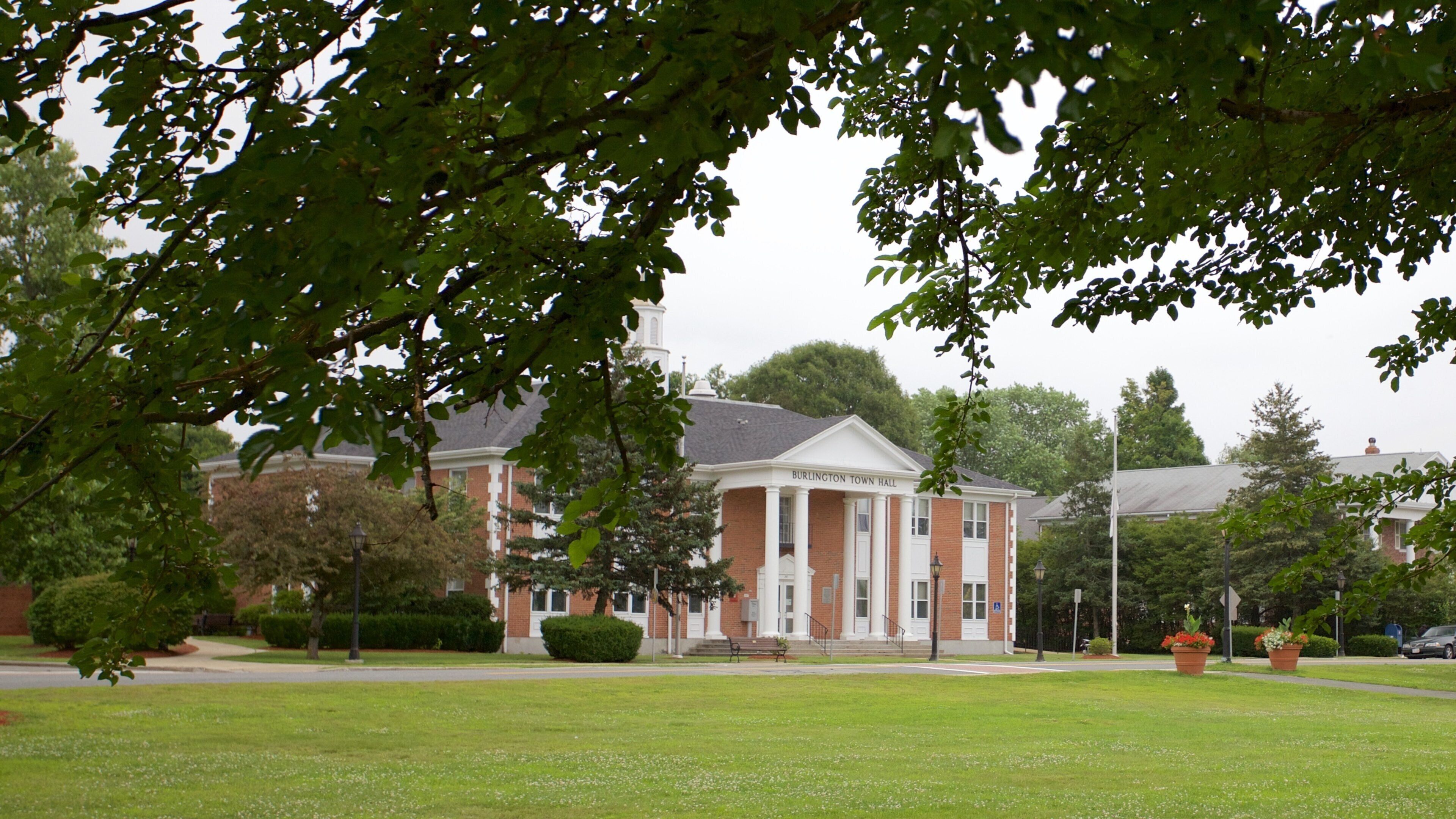 A brick building with a white facade and columns, surrounded by green grass and trees.