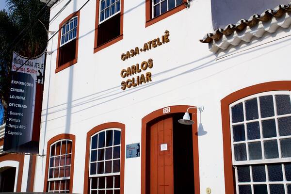 Ein Gebäude mit der Beschilderung "CASA-ATELIÊ CARLOS SCLAR" und einem Banner, das Dienstleistungen wie Kino, Tanz und Malerei auflistet.