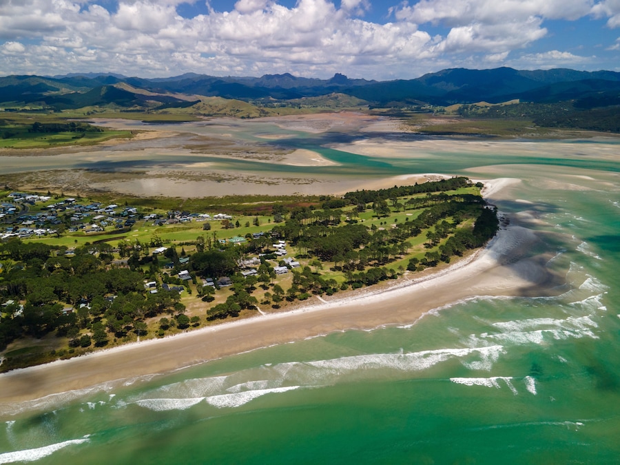 A coastal landscape with a beach, a golf course, and mountains in the background.