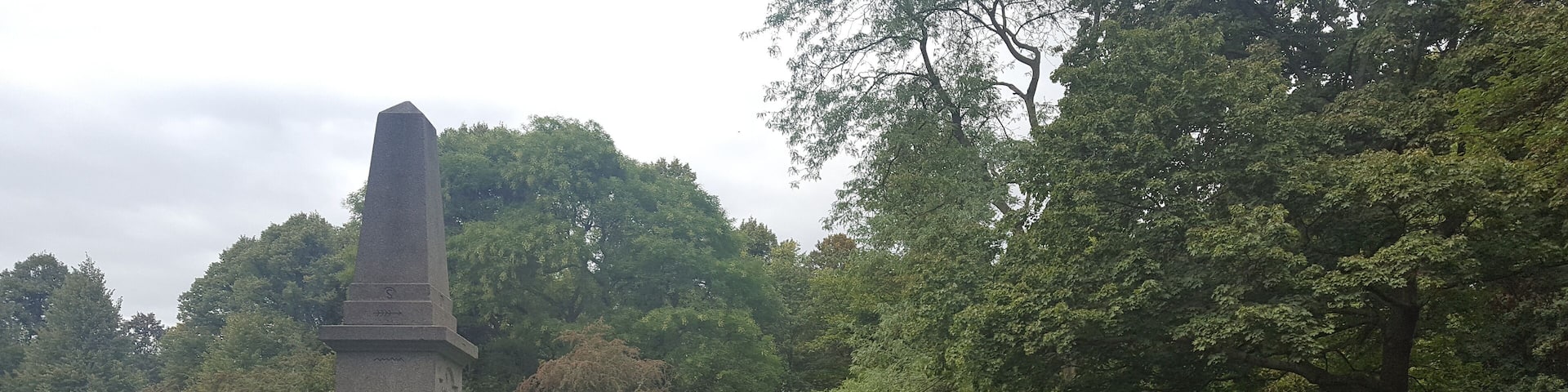 A stone obelisk and an owl statue in a park.