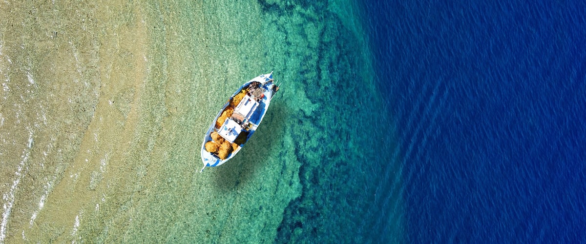 Aerial top view photo of traditional fishing boat anchored in turqoise bay and beach of Balos, Chania, Crete, Greece