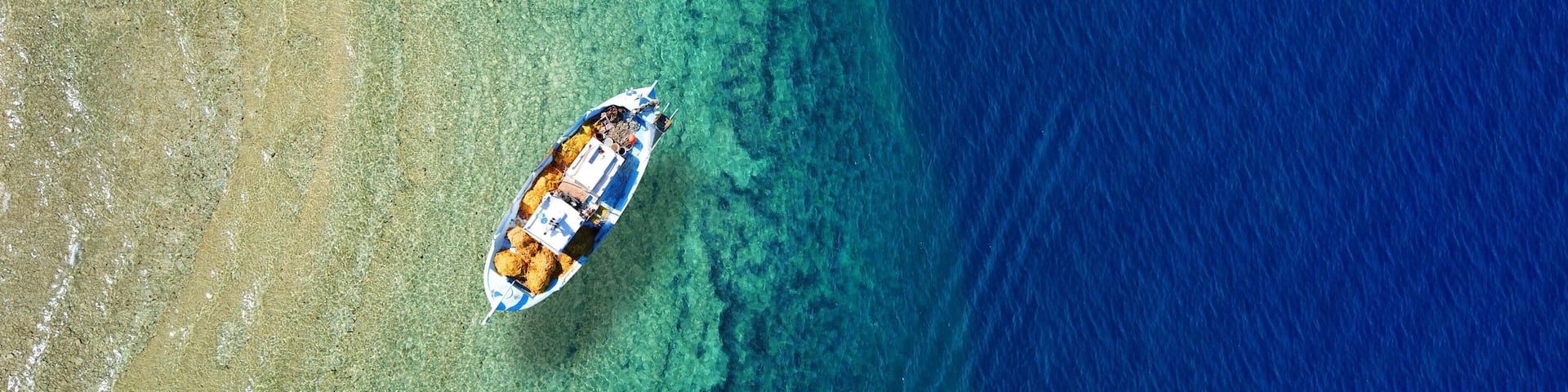 An aerial view of a boat on a clear blue sea with a sandy beach on the left.