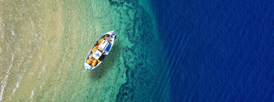 An aerial view of a boat on a clear blue sea with a sandy beach on the left.