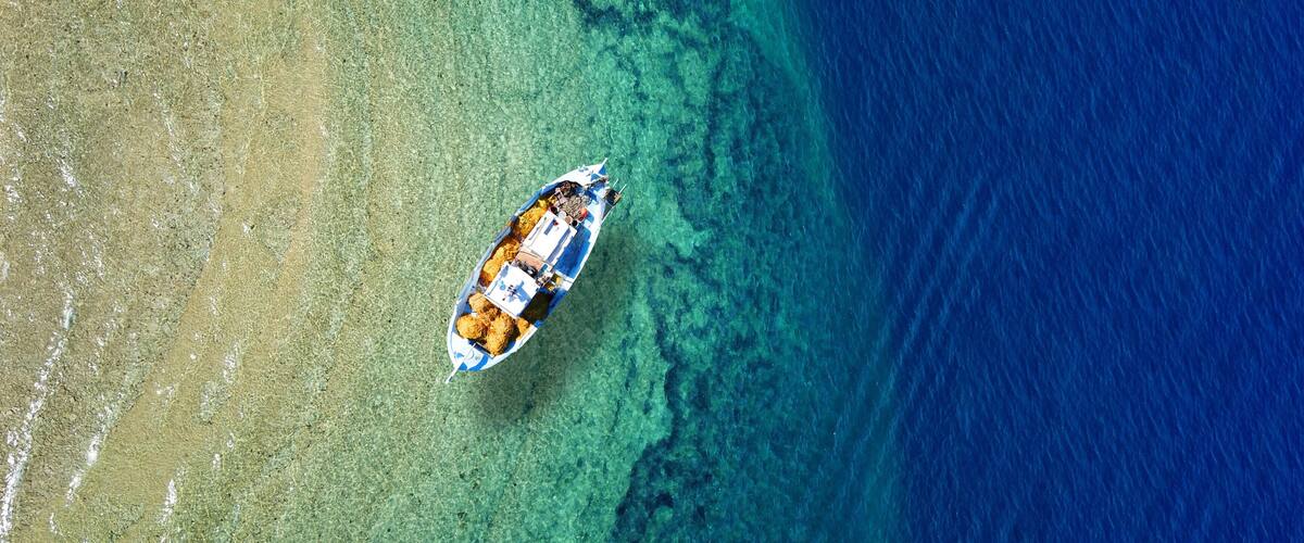 An aerial view of a boat on a clear blue sea with a sandy beach on the left.