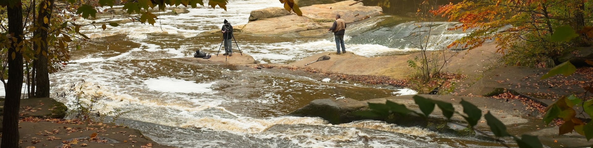 Unidentified photographer and fisherman share the boulders in the Rocky River in a northeast Ohio park