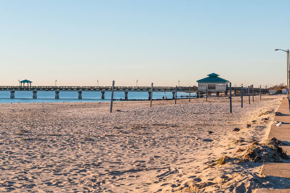Una playa con un muelle que se adentra en el agua, un pabellón y una estructura cubierta.