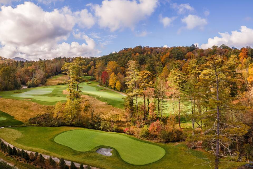 Un campo de golf rodeado de árboles de colores otoñales y un cielo despejado.