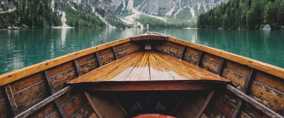 A wooden boat on a calm lake surrounded by steep, rocky mountains and dense forests.