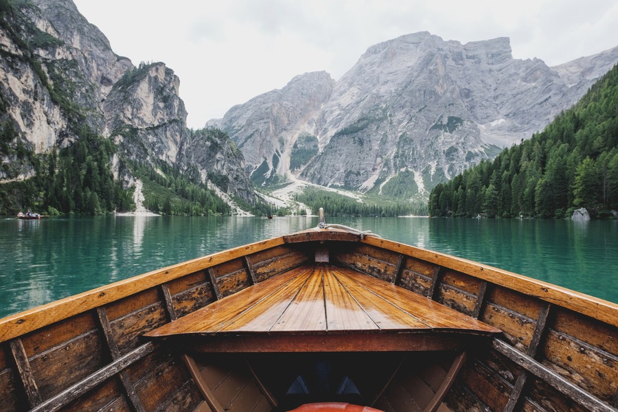 Un bote de madera en un lago tranquilo rodeado de montañas escarpadas y bosques densos.
