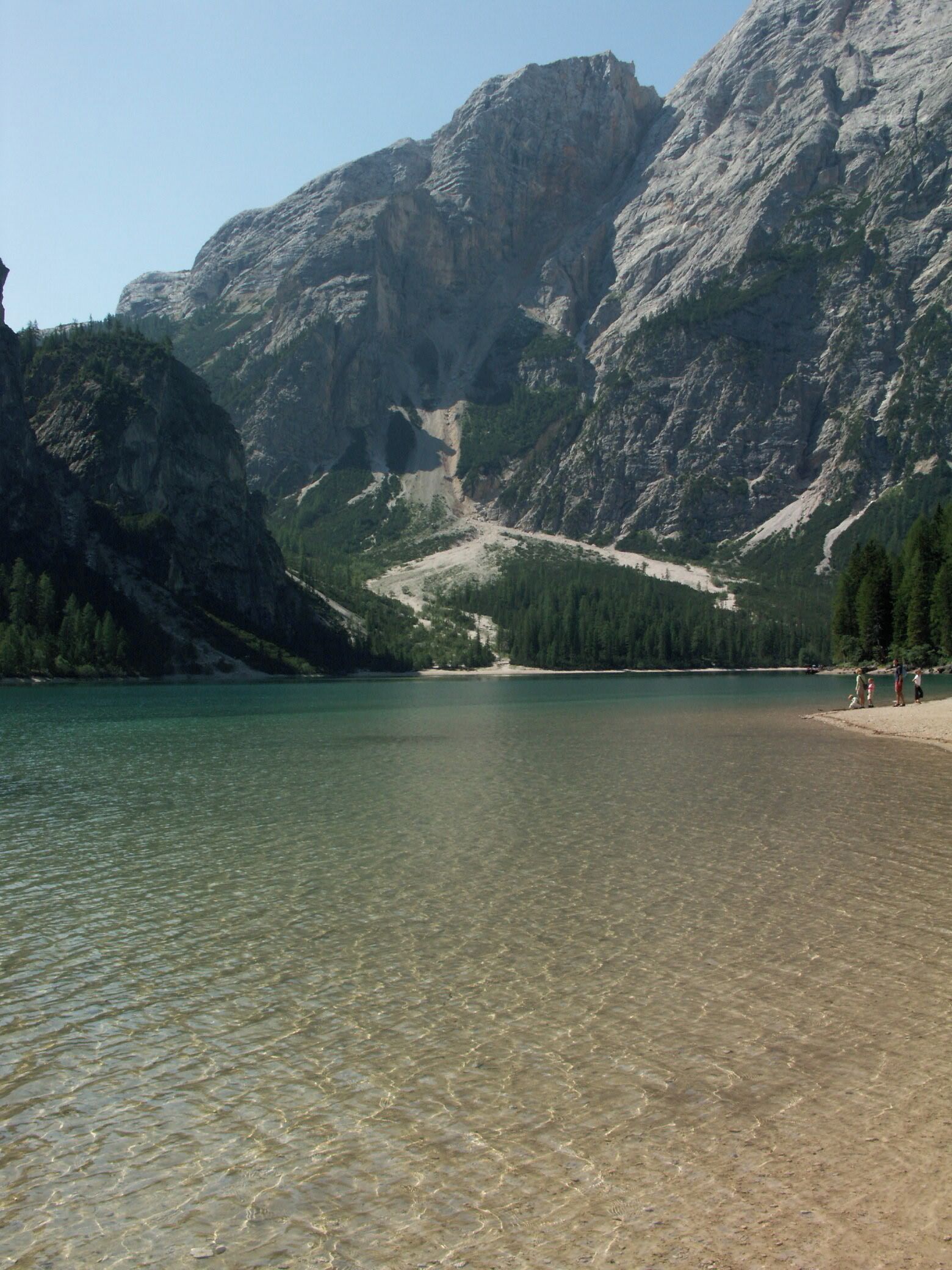 Un lago transparente rodeado de montañas rocosas y bosques densos.