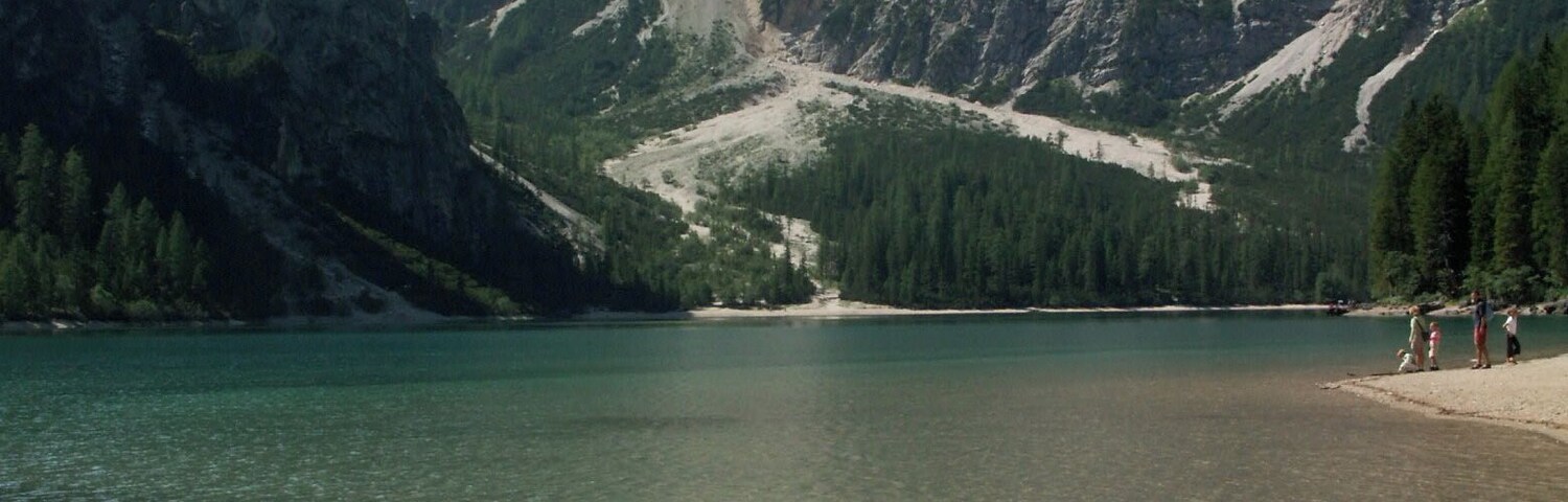 Un lago transparente rodeado de montañas rocosas y bosques densos.