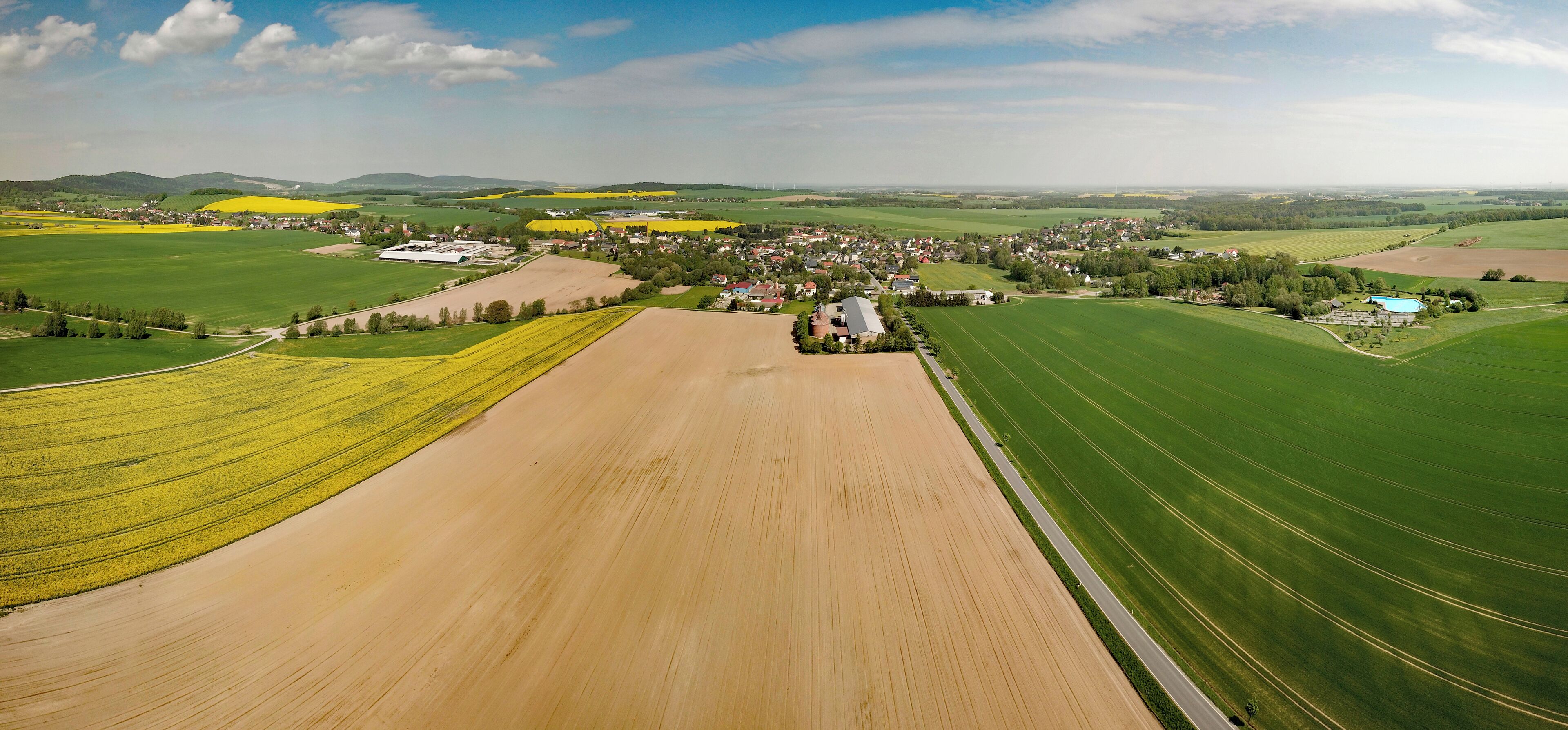 An aerial view of a rural landscape with fields, a small town, and rolling hills in the background.