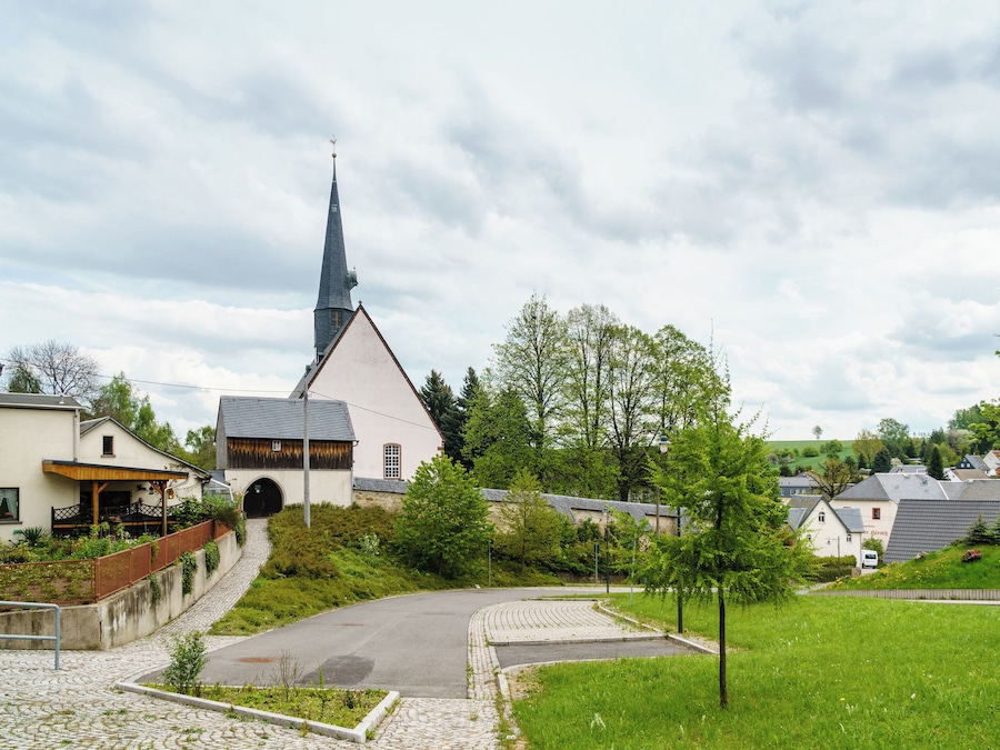 A church with a tall steeple, surrounded by houses and greenery.