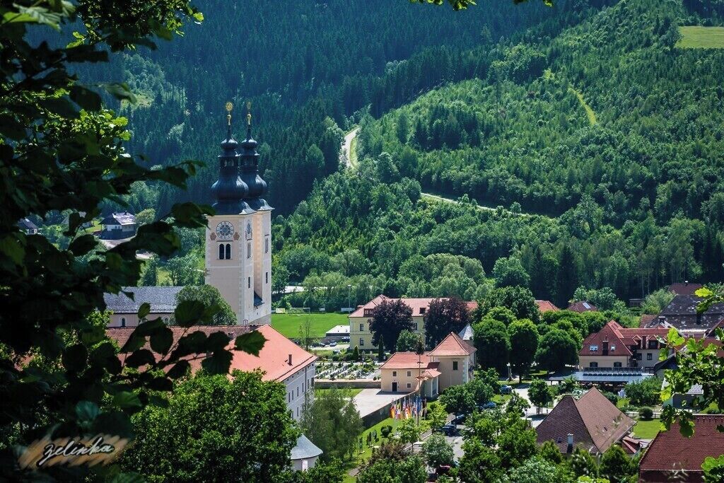 A town with a prominent church tower, surrounded by lush greenery and rolling hills.