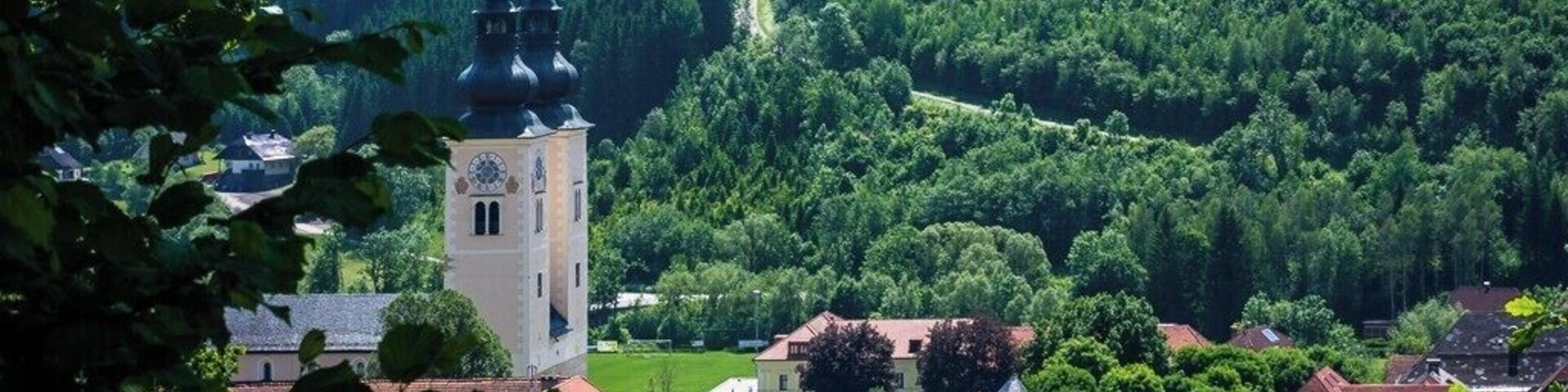 A town with a prominent church tower, surrounded by lush greenery and rolling hills.