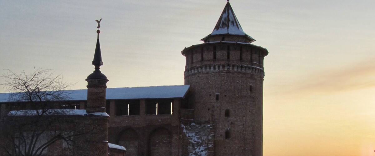 A historic brick building with a tall tower and a spire, surrounded by snow.