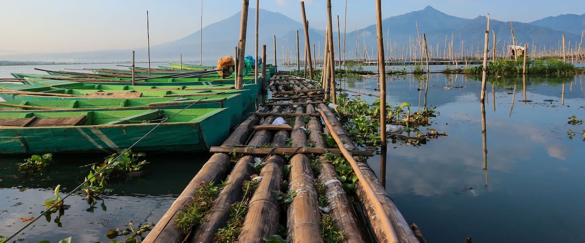 A bamboo raft docked at a calm river with mountains in the background.