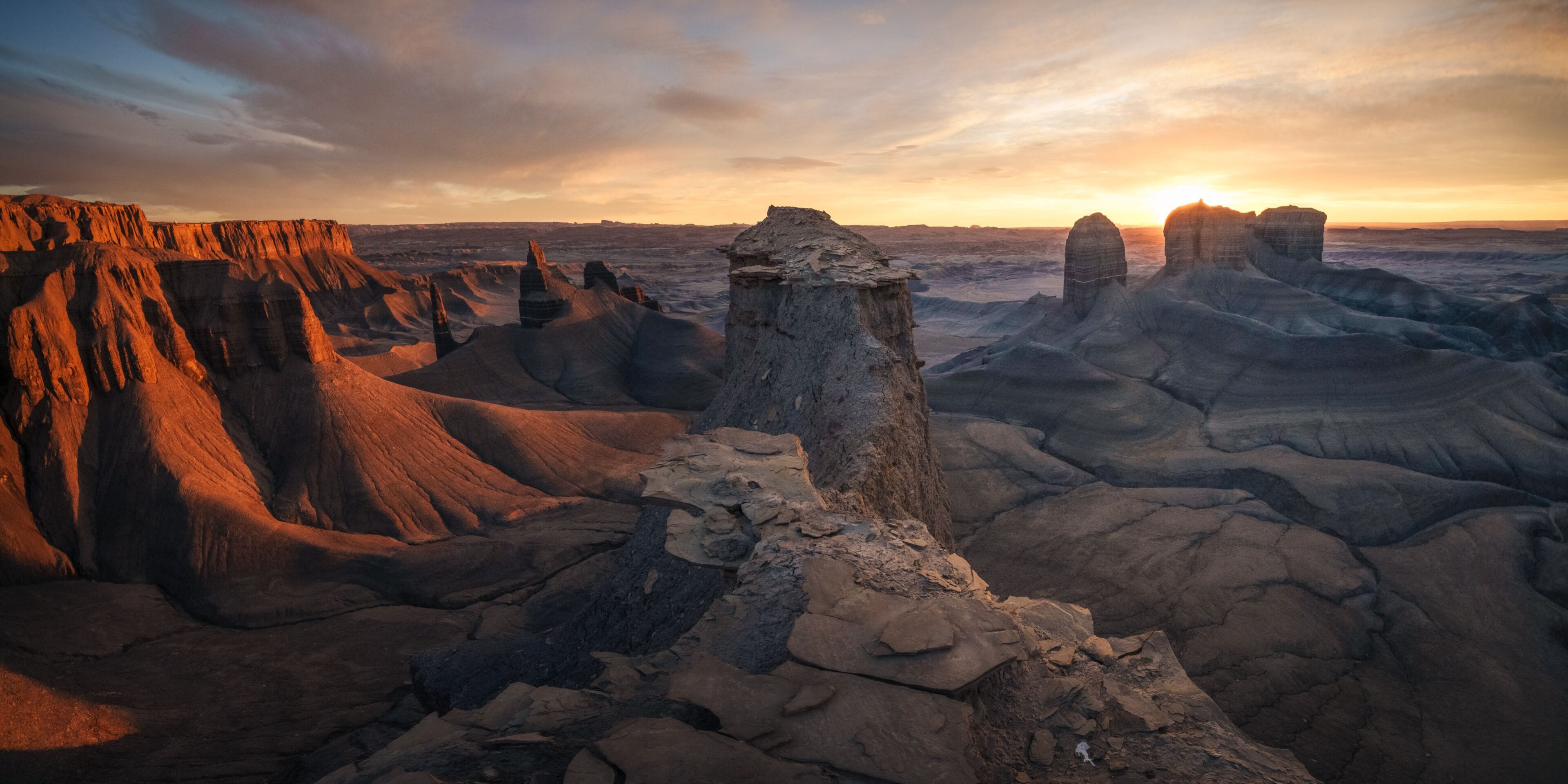Extenso paisaje desértico con formaciones rocosas destacadas y un atardecer en el fondo.