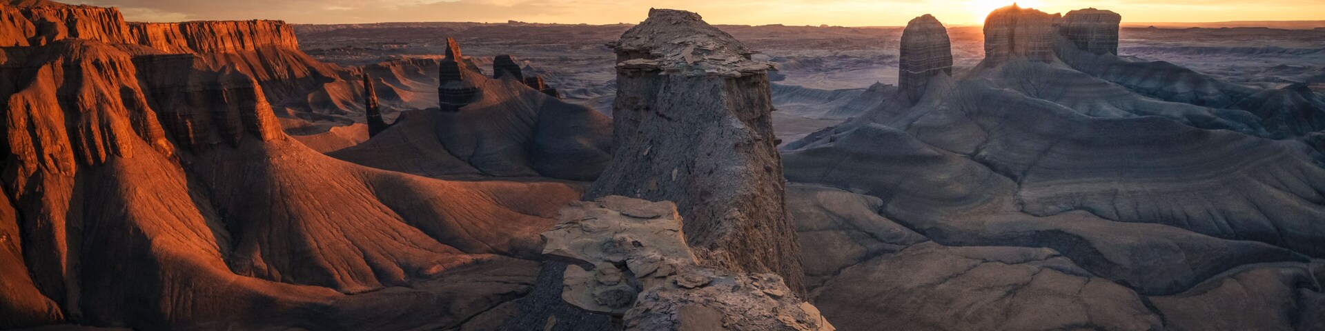 Extenso paisaje desértico con formaciones rocosas destacadas y un atardecer en el fondo.