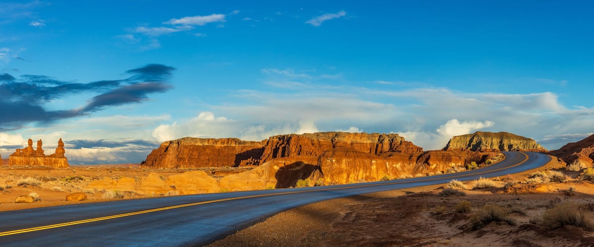 A winding road through a desert landscape with prominent rock formations and mesas.