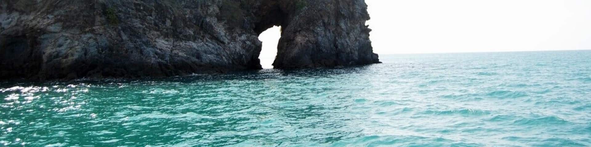 A coastal landscape with a prominent rock formation featuring a natural arch over the sea.