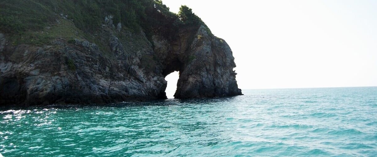 A coastal landscape with a prominent rock formation featuring a natural arch over the sea.