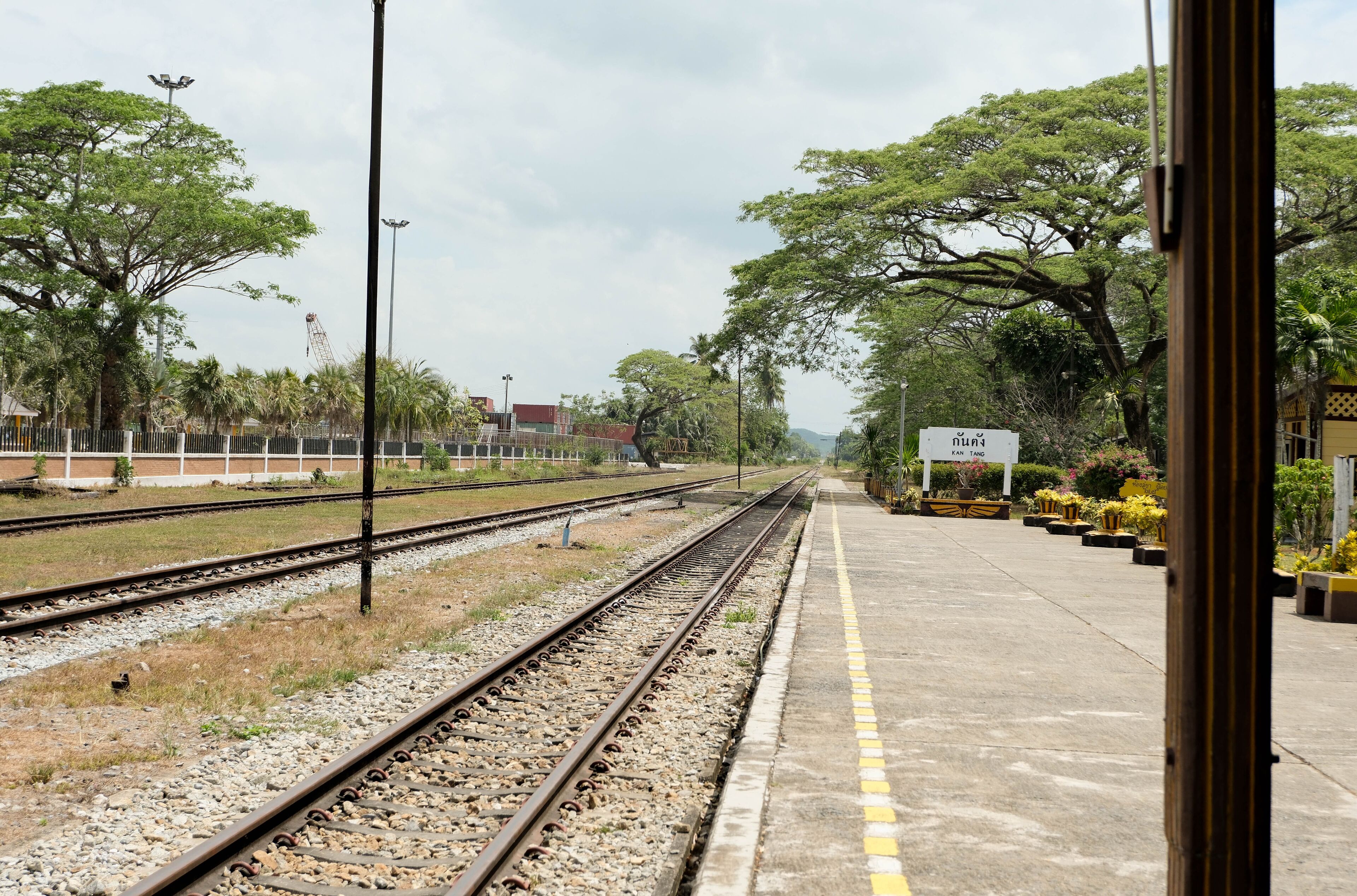 A railway station with multiple tracks, a platform, and surrounding greenery.