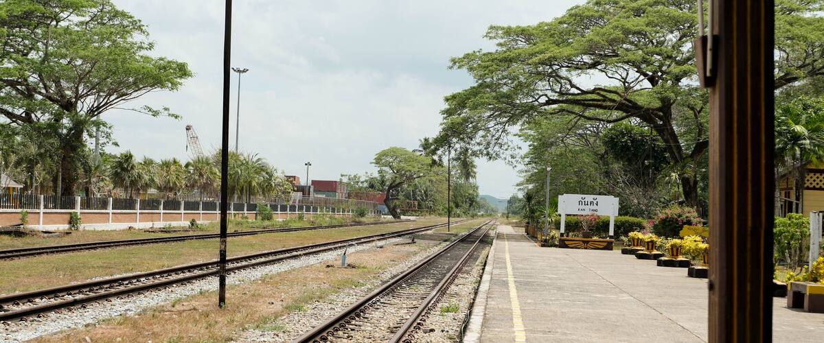 A railway station with multiple tracks, a platform, and surrounding greenery.